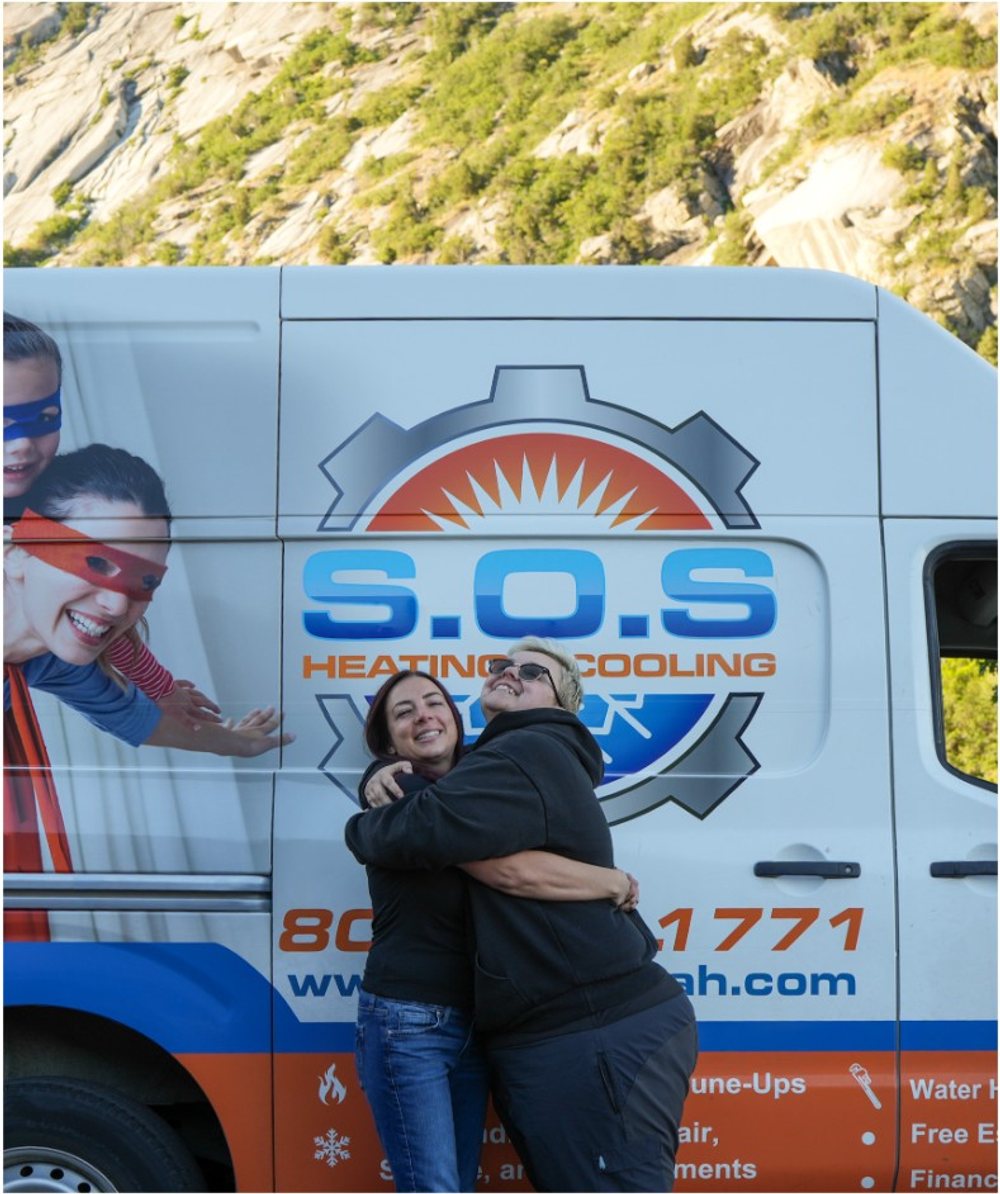 Two members of the S.O.S. dispatch team hugging in front of a company van